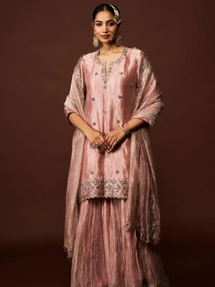 An elegant dusty pink sharara set made from a textured, shimmering fabric, featuring subtle silver embroidery around the neckline and hem.