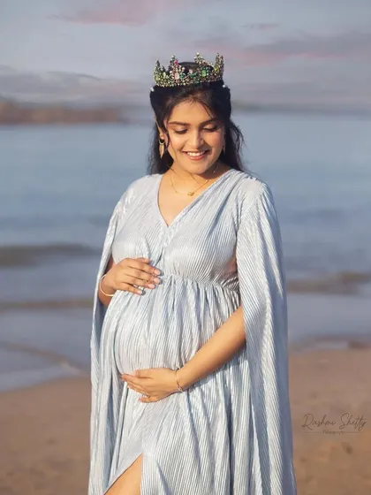 For the queen that you are. This beautiful mom-to-be is glowing in a light blue pleated maternity dress with an elegant cape. It's a perfect choice for a serene beach photoshoot, combining comfort with a regal, ethereal look.
