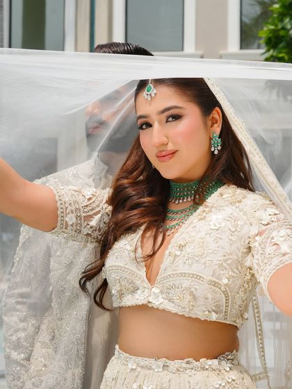 A playful and romantic shot of the bride under her veil. Her makeup is fresh and natural, with a focus on glowing skin that looks luminous even in the bright, outdoor light.