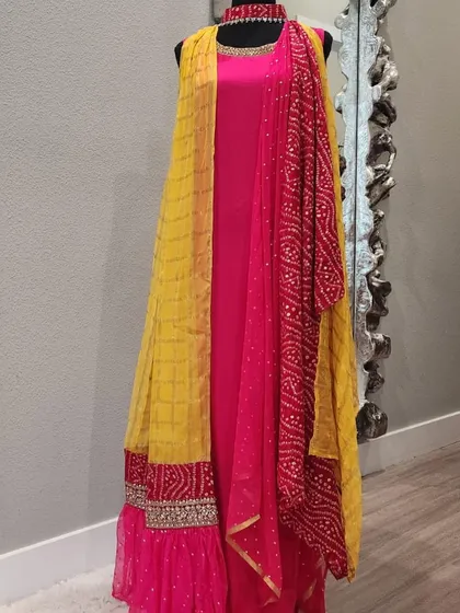 A stunning fusion gown in bright pink and yellow. This piece features a ruffled skirt, an attached Bandhani-print dupatta, and an embellished border, combining several beautiful elements into one look.