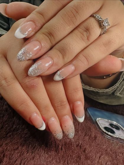 Another take on the glitter French. This set features a half-moon design with white tips and a cascade of silver glitter on almond-shaped nails.