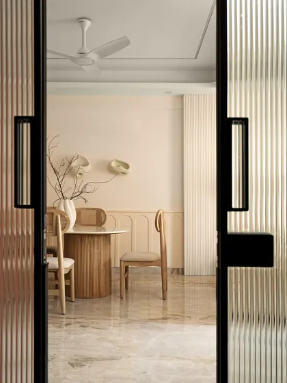 This dining room embraces the quiet elegance of Wabi-Sabi design. Peeking through fluted glass doors, the space is intentionally minimal and calm, using honest materials and warm light to create a peaceful setting for connection and shared meals.