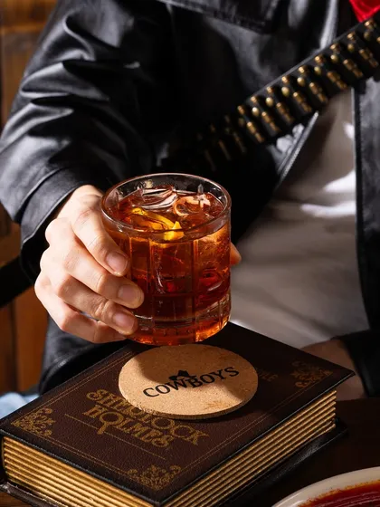 A close-up of a whiskey cocktail, styled with a western theme. The props and lighting are chosen to match the bar's unique concept.