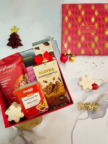 A festive shot of the Joy of Christmas Gift Box, open to reveal the treats inside. It includes almond brittle, butterscotch dip sticks, and cranberry almond crisps.