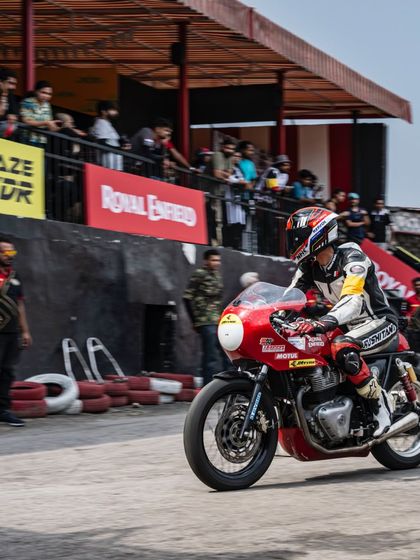 A rider exits a corner at the RE GT Cup Zonal Selection in Delhi, with the crowd watching from the stands.