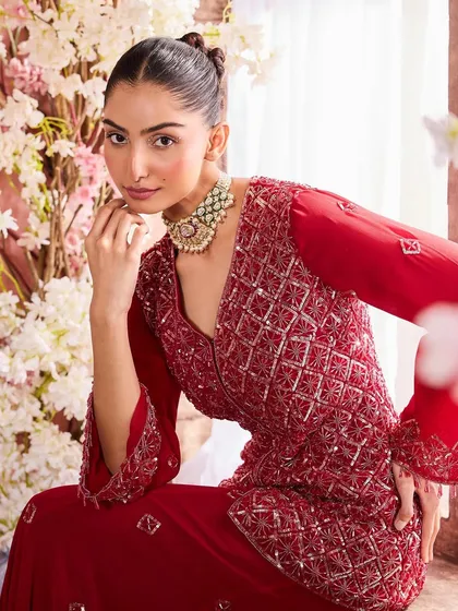 A model in a rich red embroidered outfit. The makeup is warm and defined, with a focus on the eyes and a perfectly sculpted complexion to match the regal feel of the garment.