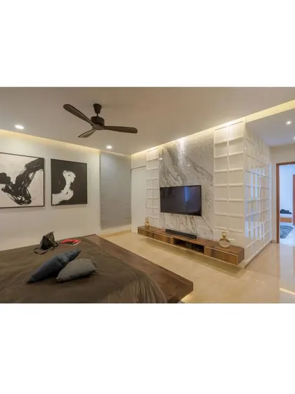 The master bedroom in Athulyam is a composition of simple forms and elegant materials. A floating bed and a low-profile media unit keep the space feeling open, while a textured partition wall adds visual interest and separates the sleeping area from the ensuite.