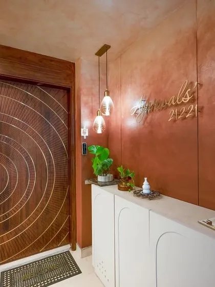The entryway to a home sets the first impression. This design features a modern, backlit panel with a custom nameplate, a sleek white console, and a beautifully crafted wooden door with concentric circle details.