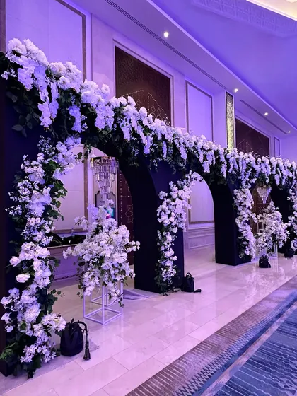All white for a finale reception. This grand entrance features a series of black arches adorned with an abundance of pristine white flowers, creating a dramatic and elegant statement. 🤍