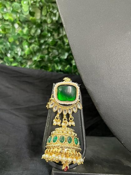 A unique earring with a large square green stone and a jhumka drop with smaller green stones.