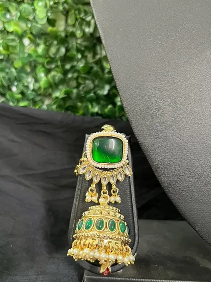 A unique earring with a large square green stone and a jhumka drop with smaller green stones.