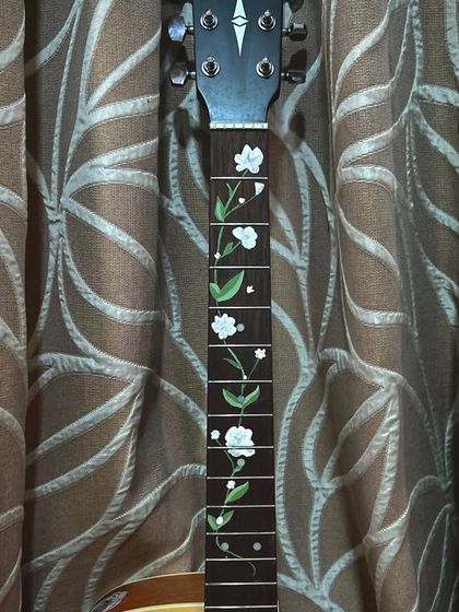 A full view of the painted guitar neck. The white flowers and green leaves create a beautiful contrast against the dark wood of the fretboard.