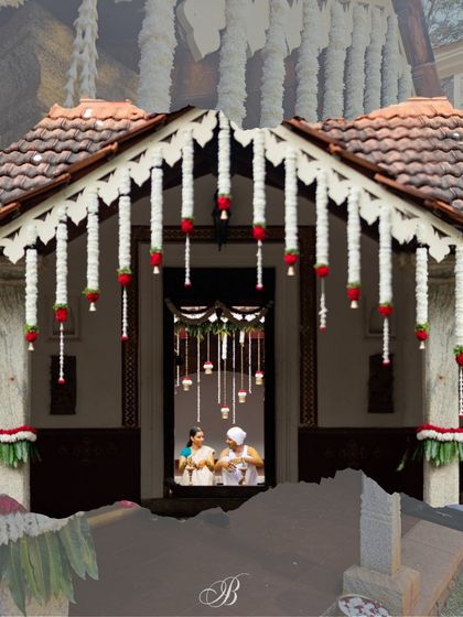 The couple is seen through the entrance of the house during their Vara Puje. The decor, with its hanging tuberose and red rose garlands, creates a beautiful and traditional welcome.