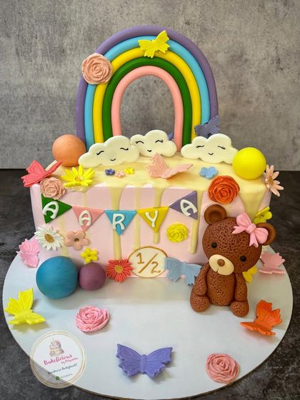 Celebrating a half-birthday with this adorable rainbow and teddy bear cake. It's packed with cute details like fondant flowers, butterflies, and a personalized bunting for baby Arya.