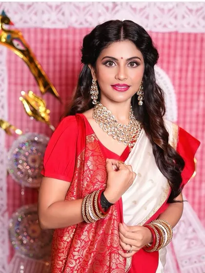A festive Bengali look for a special occasion. The makeup features a bright lip and defined eyes, complementing the traditional red and white saree.
