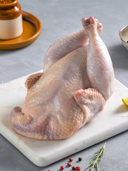 A whole raw chicken, cleaned and ready for cooking, presented on a marble slab with simple seasoning.