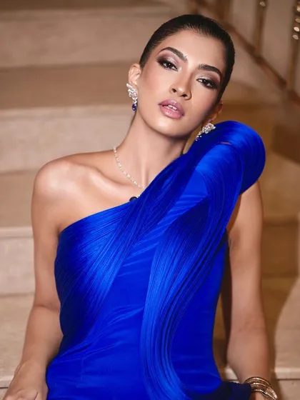 A striking pose on the stairs showcases this avant-garde look. The makeup is sharp and artistic, complementing the structural elegance of the royal blue gown.