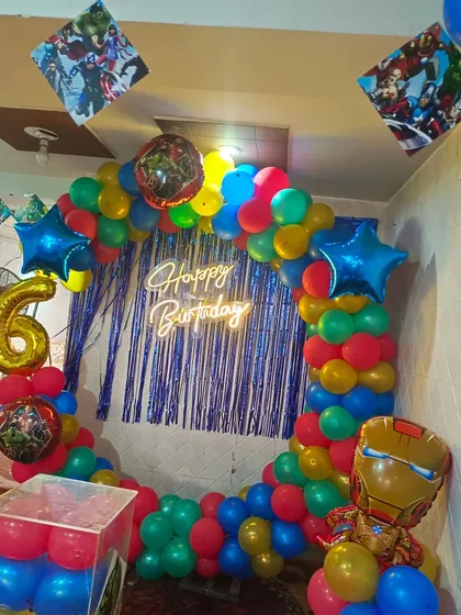An action-packed Avengers theme for a 6th birthday. This decoration includes a colorful balloon ring, character foil balloons like Iron Man and Hulk, and a blue shimmer curtain.