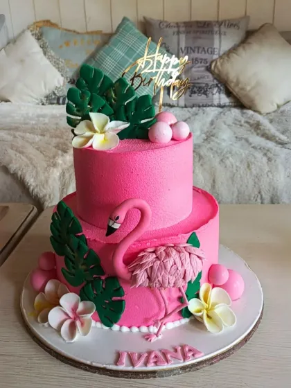 A vibrant two-tier tropical cake in bright pink, featuring a graceful flamingo, monstera leaves, and plumeria flowers.