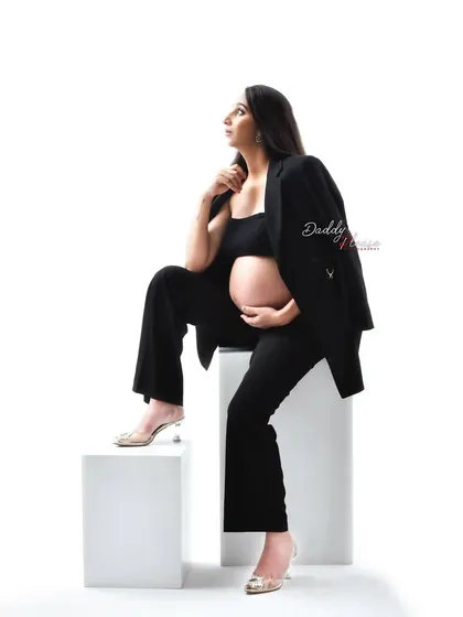 A full-body shot of the modern pantsuit look. The mom-to-be is posed on white blocks, showcasing a confident and contemporary approach to maternity photography.