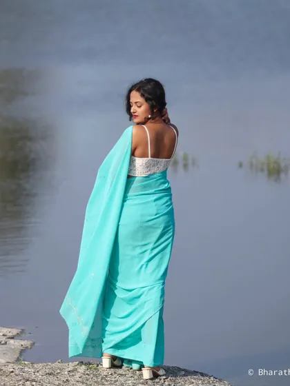 A back-profile shot of the model looking out over the water. This angle highlights the modern, strappy blouse paired with the traditional saree.