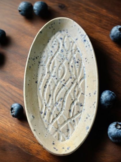 An oval platter with a delicate, speckled glaze over a carved, flowing pattern. This versatile piece is perfect for serving snacks or as a beautiful catch-all tray for your keys and jewelry.