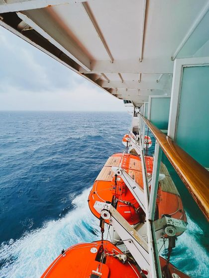 A view from the side of the cruise ship, showing the lifeboats and the churning water below, giving a sense of movement and scale.