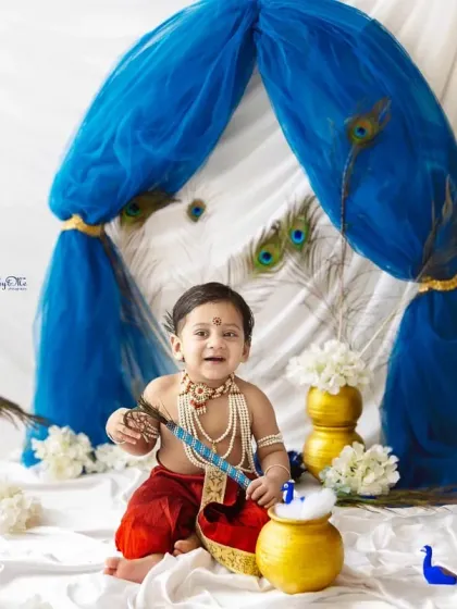 This happy little Kanha is playing with a pot of 'butter'. The whole setup, with peacock decor and golden matkas, is designed to celebrate the spirit of Janmashtami.