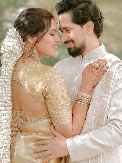 A romantic couple shot. The bride is wearing a beautiful golden saree, and her hair is styled in a traditional South Indian braid with a long gajra.
