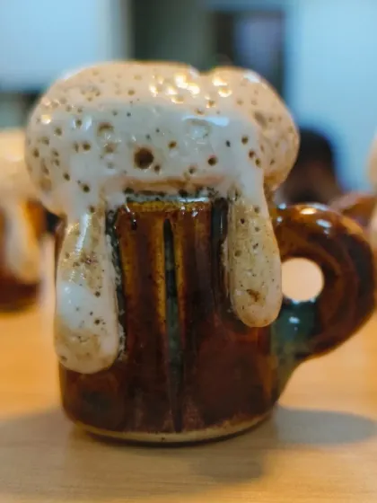 A close-up of a miniature ceramic beer mug, complete with overflowing foam. This piece, made by our student Sejal, is a testament to the fun and creativity that is possible with clay.