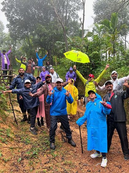 A vibrant and energetic group photo on a muddy trail, with everyone celebrating the rain and the trek.