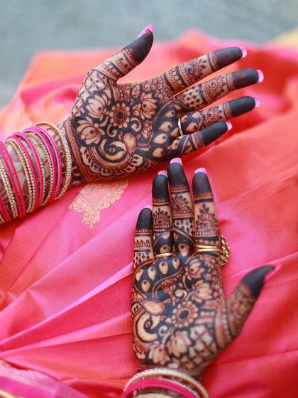A close-up of the back of the hands, featuring intricate peacock and floral designs with solid fingertips.