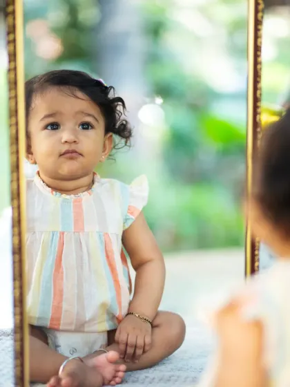 Using a mirror as a prop can create fascinating and introspective portraits. Here, a baby girl calmly observes her own reflection during an outdoor session.