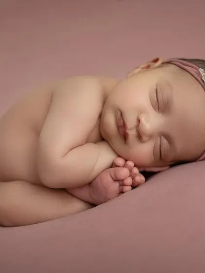 A full body view of the 'taco' pose, showing how the baby's feet are tucked in cozily. The soft pink color palette is perfect for a baby girl's newborn session.