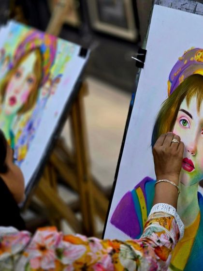 An artist at work, applying layers of soft pastels to her portrait. This over-the-shoulder view gives a glimpse into the hands-on process of creating with this vibrant medium.