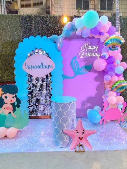 A vibrant mermaid-themed party with a blue shimmer wall and character cutouts. The decor includes a cute starfish prop and a balloon garland in ocean colors.
