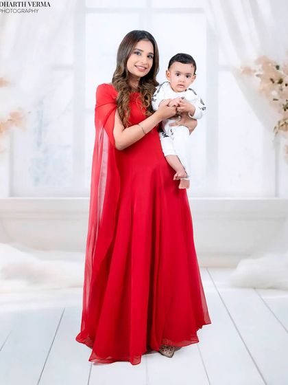 An elegant full-length portrait of a mother in a stunning red gown holding her baby. The soft, dreamy background enhances the artistic feel.
