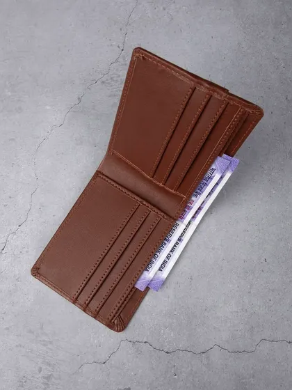 An open view of a brown leather wallet, displaying its multiple card slots and cash compartment with currency notes.