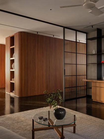 This image shows the interplay of spaces in 'Rambagh', with the living area, home office, and dining room defined by glass partitions and our signature curved wood element. This approach creates distinct functional zones without sacrificing the home's open and airy feel.