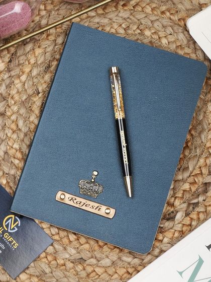 A blue personalized leather diary and pen set with a crown charm.
