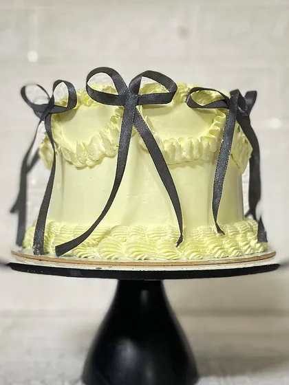 The elegant silhouette of the yellow bow cake on a black stand.
