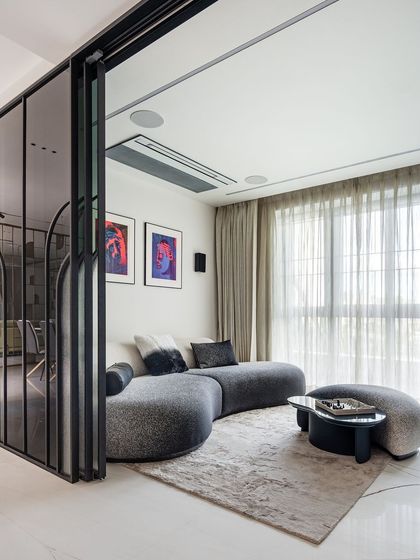 In this informal living space, a curved, textured sofa creates a cozy and conversational nook. The area is separated by a fluted glass and metal partition, which provides a sense of privacy without closing off the room, maintaining an open and modern feel.