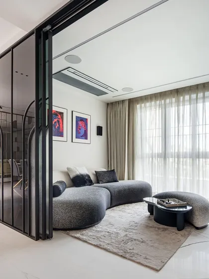 In this informal living space, a curved, textured sofa creates a cozy and conversational nook. The area is separated by a fluted glass and metal partition, which provides a sense of privacy without closing off the room, maintaining an open and modern feel.
