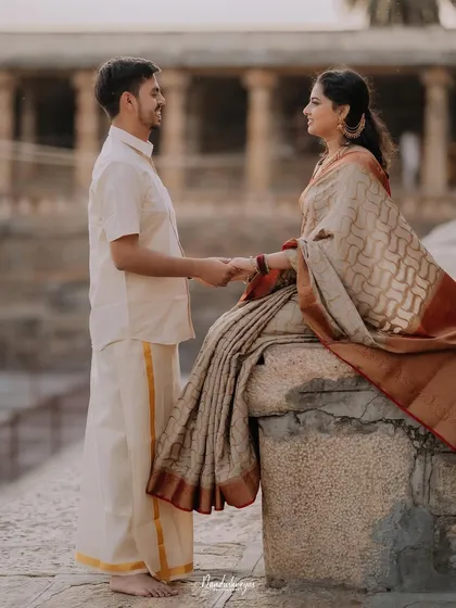 A classic romantic pose, with the groom standing and holding the hand of his bride-to-be, who is seated on a stone ledge.