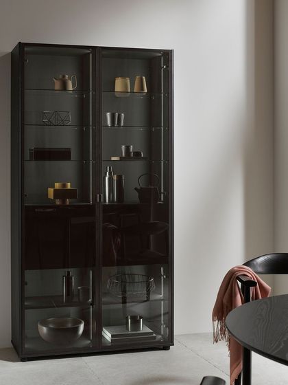 A freestanding glass display cabinet in a matching black finish complements the kitchen, providing additional storage and continuing the elegant aesthetic into the dining area.