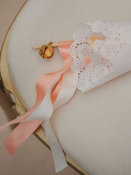 A close-up of a guest favor: a paper cone for petal tossing, attached to a ribbon wand with a tiny bell. It's a multi-sensory detail that delights guests.