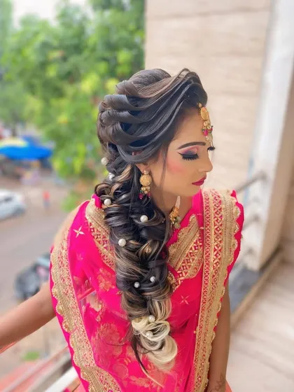 A glamorous and intricate braided hairstyle perfect for a sangeet or reception. This look features a combination of twists and a long, flowing braid decorated with pearls, with soft highlights adding dimension.