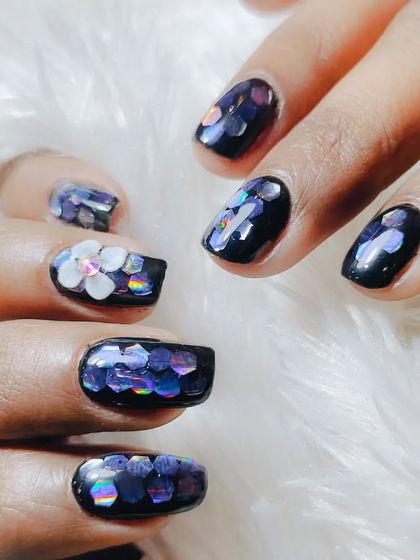 A dark and dreamy design featuring a black base with iridescent, flower-shaped glitter pieces and a 3D white flower accent.