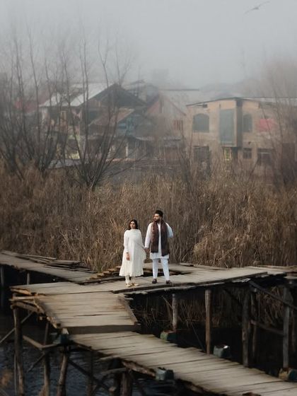 A couple stands together on a wooden pier, surrounded by the rustic charm of a village on Dal Lake. This image captures a sense of quiet togetherness and the timeless beauty of Kashmir.