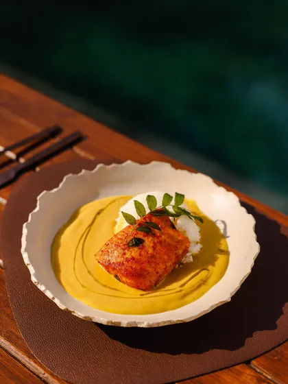 A beautifully presented fish dish with a vibrant yellow sauce, served by the tranquil waters of the pool.